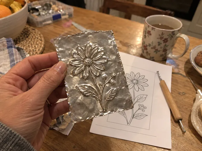 A first handmade metal piece held up at a kitchen table
